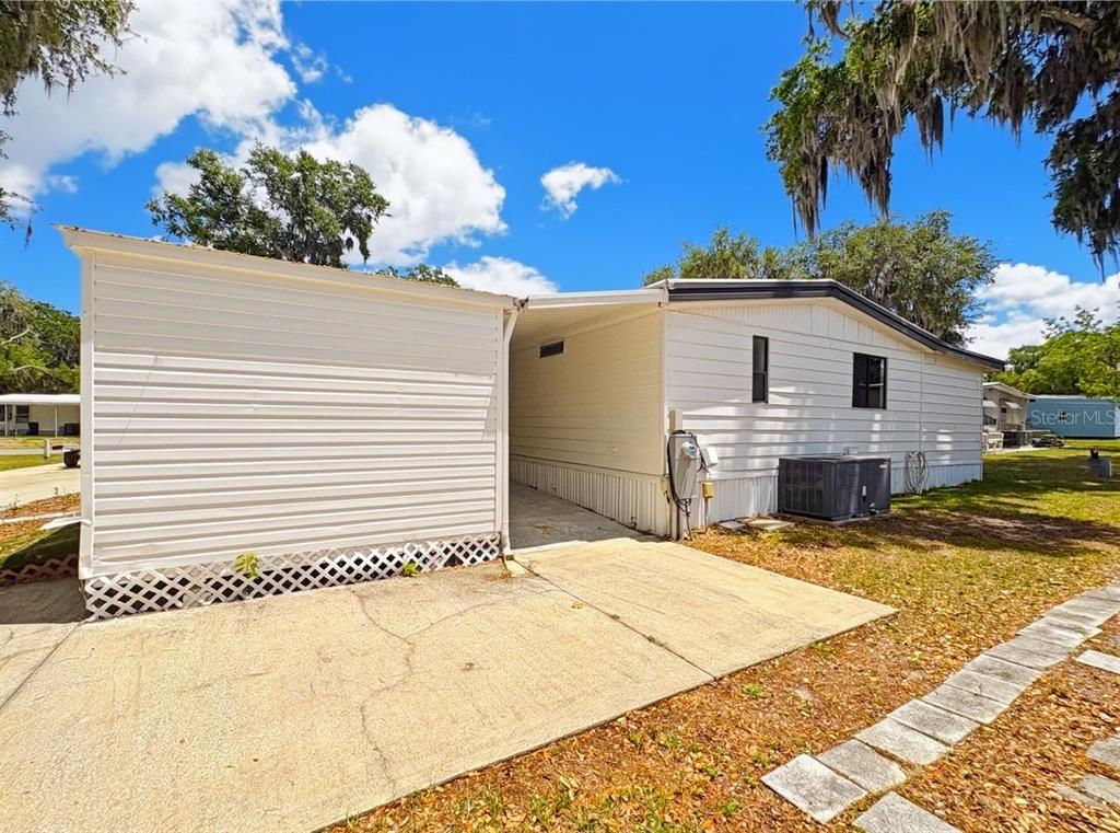 The exterior of a white mobile home features a carport and a concrete driveway — 4 E QUAIL RUN, WILDWOOD, FL
