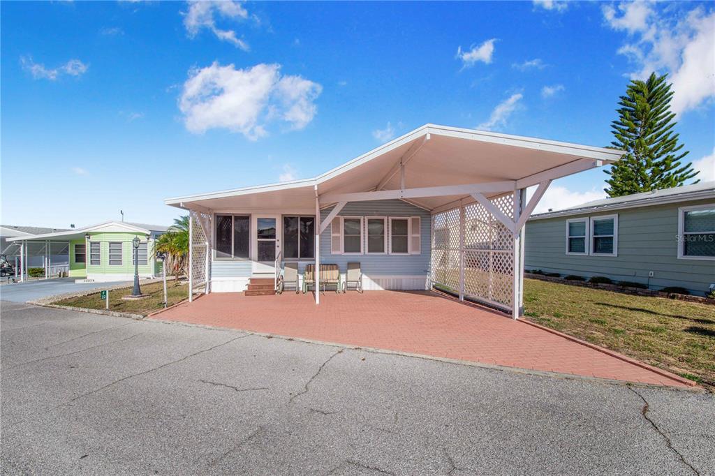 A light blue mobile home features a large attached carport and a red brick driveway — 251 PATTERSON ROAD UNIT F22, HAINES CITY, FL