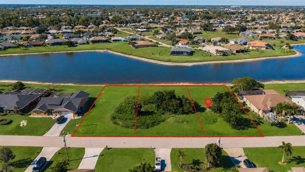 An aerial view shows three adjacent vacant lots bordering a lake in a residential neighborhood — 2369 SOFIA LANE, PUNTA GORDA, FL