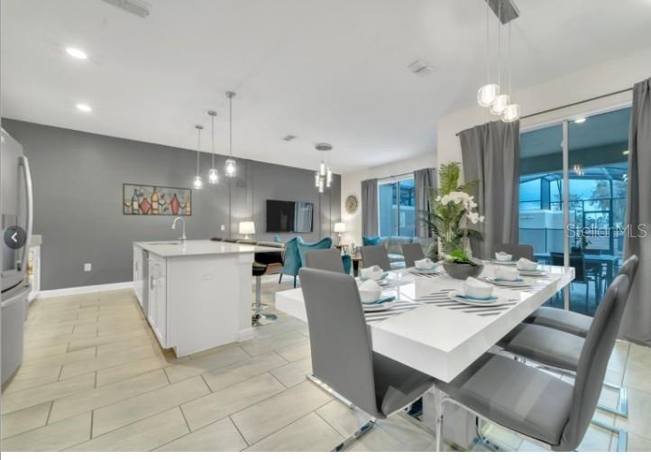 A modern open-concept kitchen and dining area features a white island, gray walls, and tile flooring — 4983 WINDERMERE AVENUE, KISSIMMEE, FL