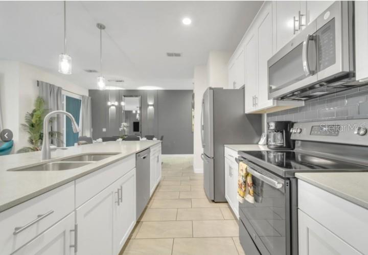 A modern kitchen features white cabinets, stainless steel appliances, a center island, and tile flooring — 4983 WINDERMERE AVENUE, KISSIMMEE, FL