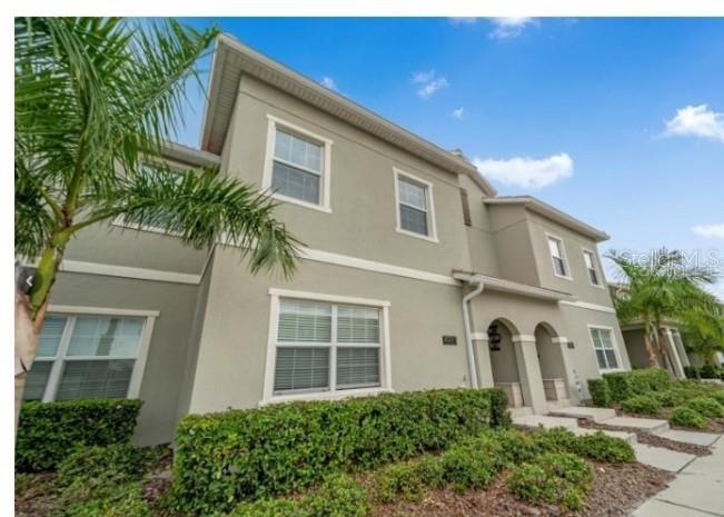 A two-story beige stucco townhouse exterior features a palm tree and manicured green hedges — 4983 WINDERMERE AVENUE, KISSIMMEE, FL