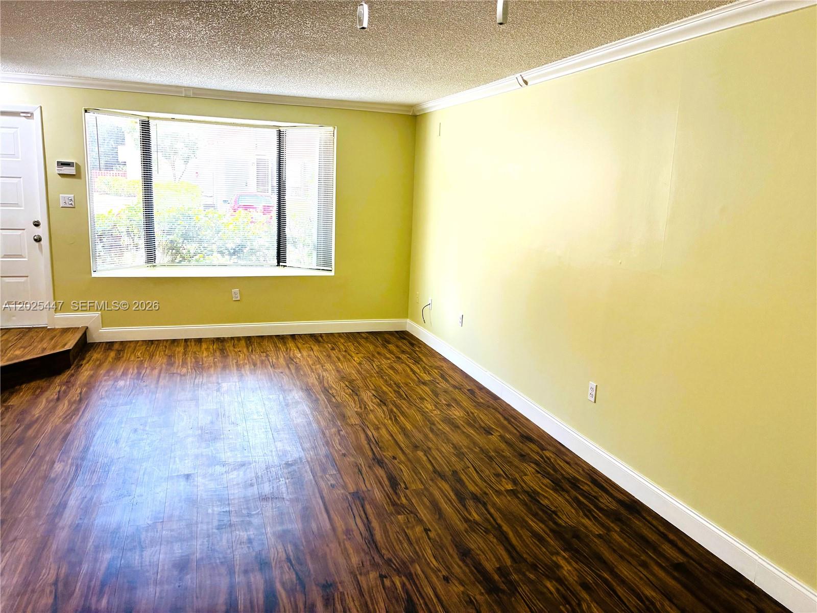 An empty room features light yellow walls, dark wood-look flooring, and a large bay window — 7796 SW 102nd Ln, Miami FL 33156, MIAMI, FL