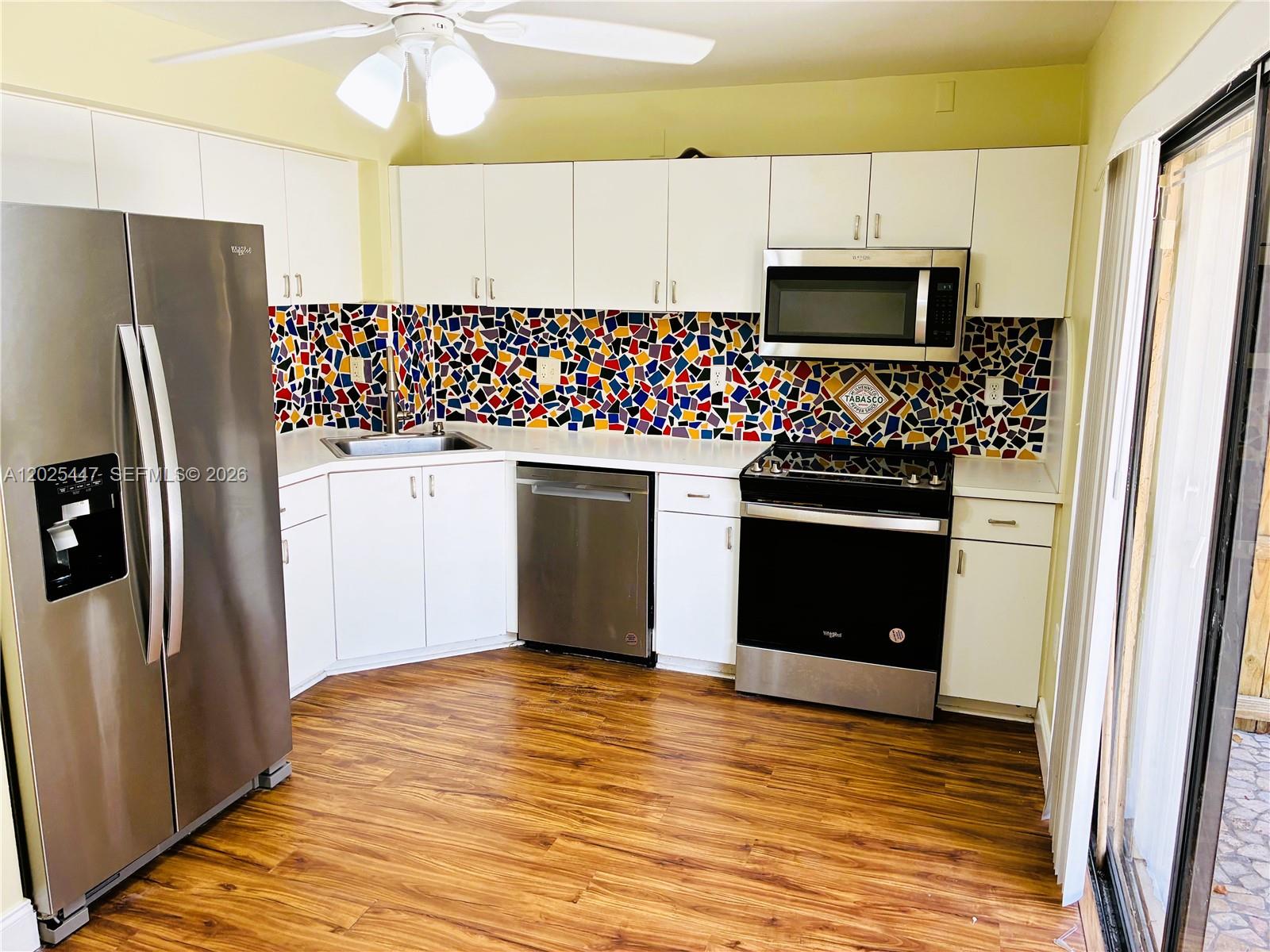 A kitchen features white cabinets, stainless steel appliances, and a colorful mosaic tile backsplash — 7796 SW 102nd Ln, Miami FL 33156, MIAMI, FL