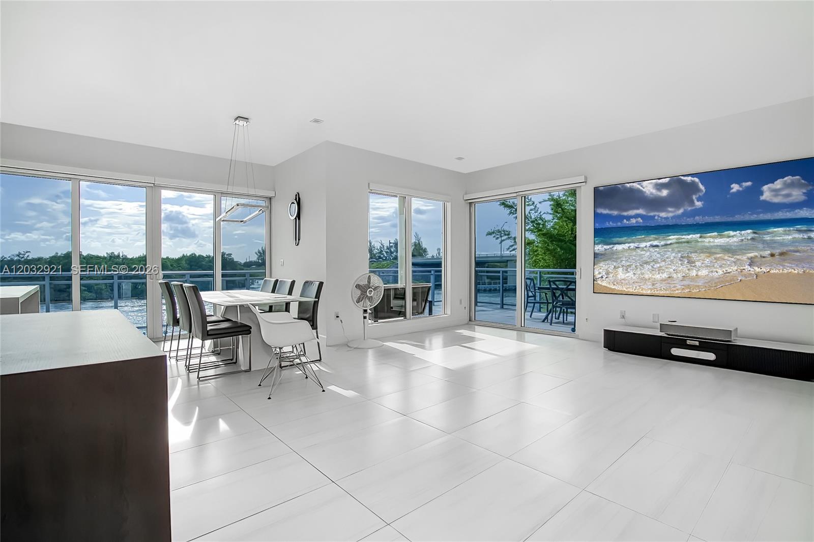 A bright living and dining area features white tile floors, large windows, and balcony access — HOLLYWOOD, FL
