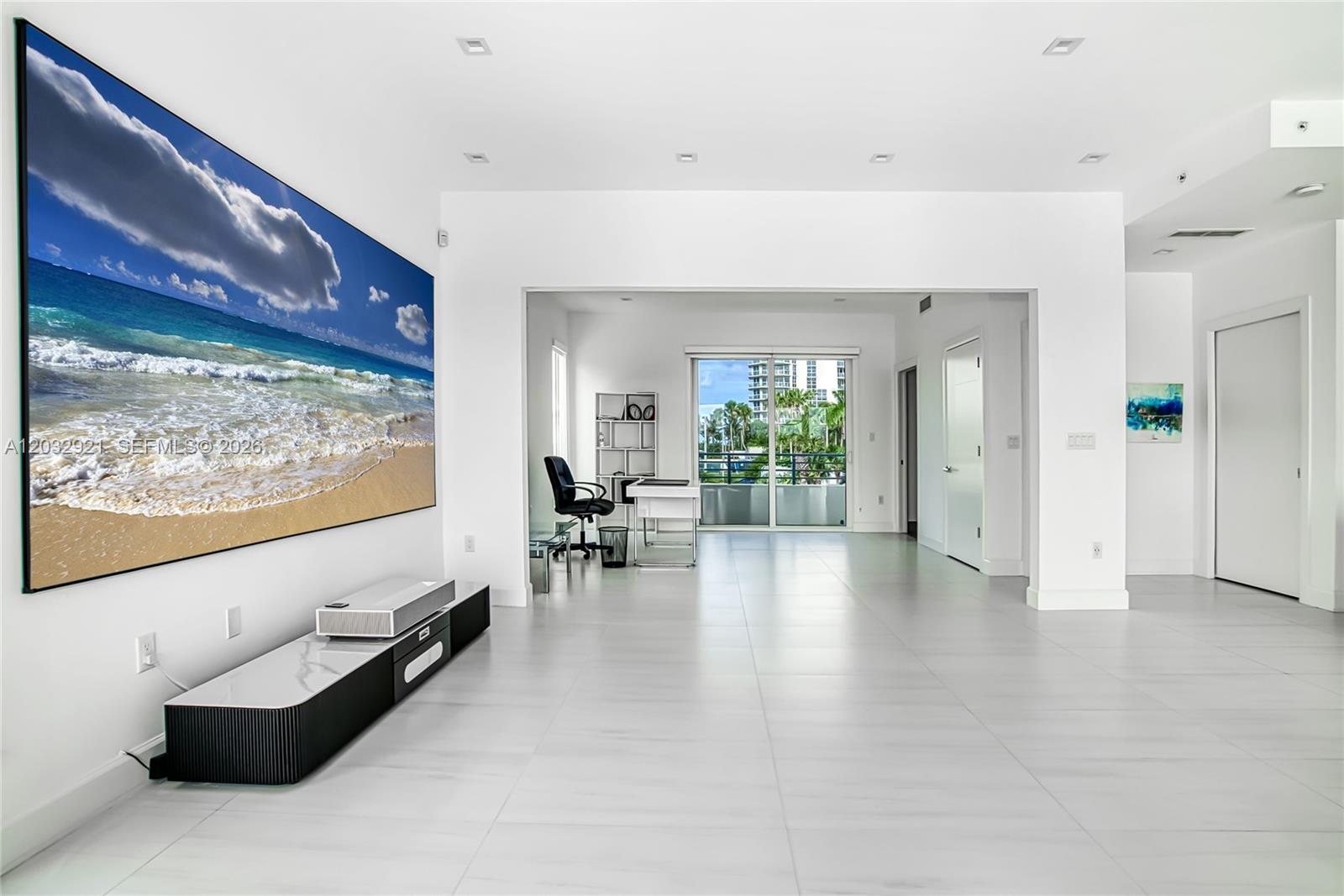 A minimalist living room features a large projection screen, white tile floors, and an office area — HOLLYWOOD, FL