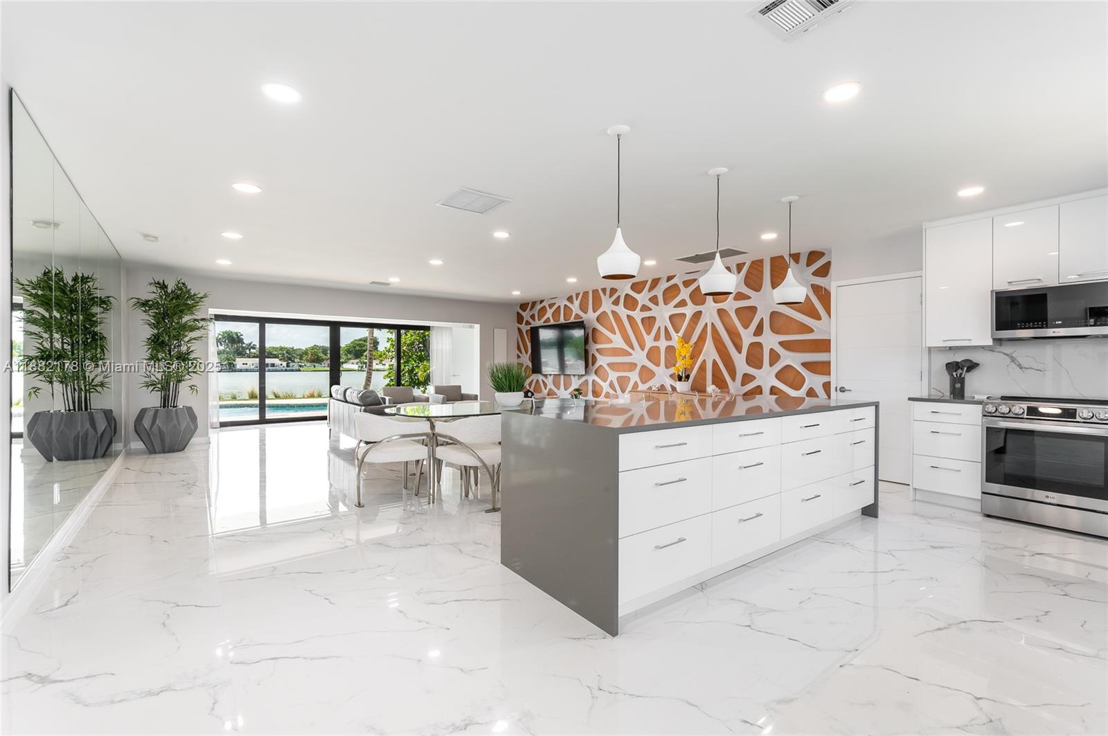 A modern kitchen and dining area features a large island, marble floors, and waterfront views — 21230 NE 25th Ct, Miami FL 33180, MIAMI, FL