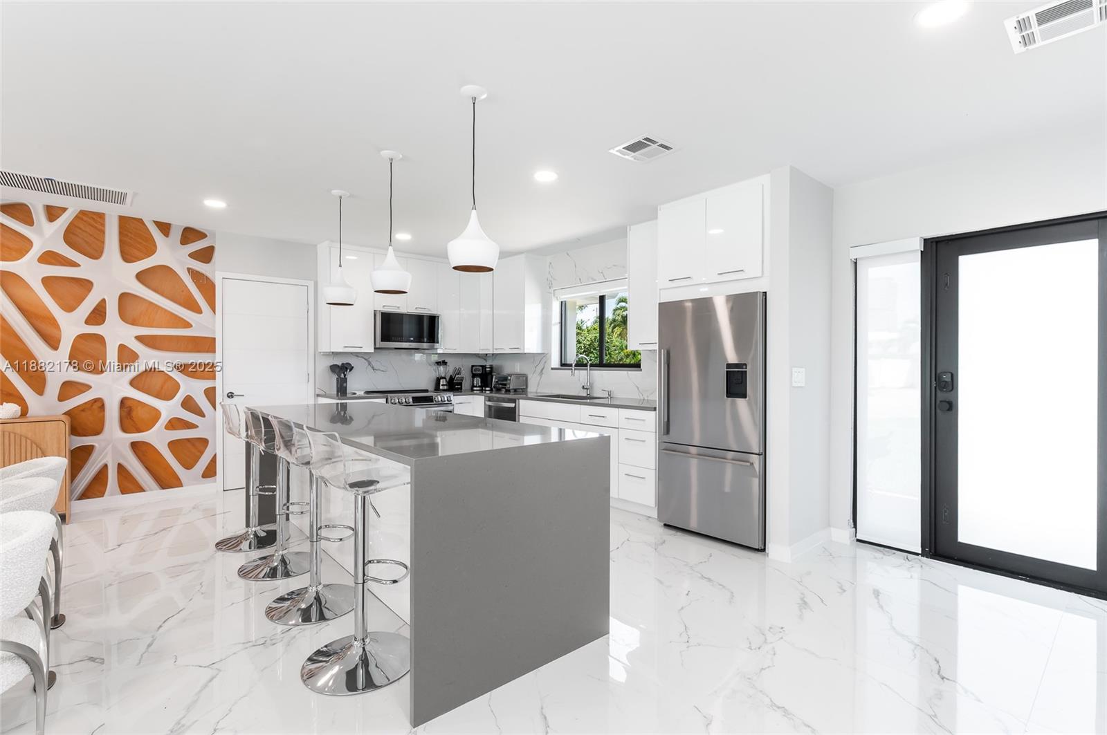 A modern kitchen features a gray waterfall island, white cabinetry, and a decorative wood wall — 21230 NE 25th Ct, Miami FL 33180, MIAMI, FL