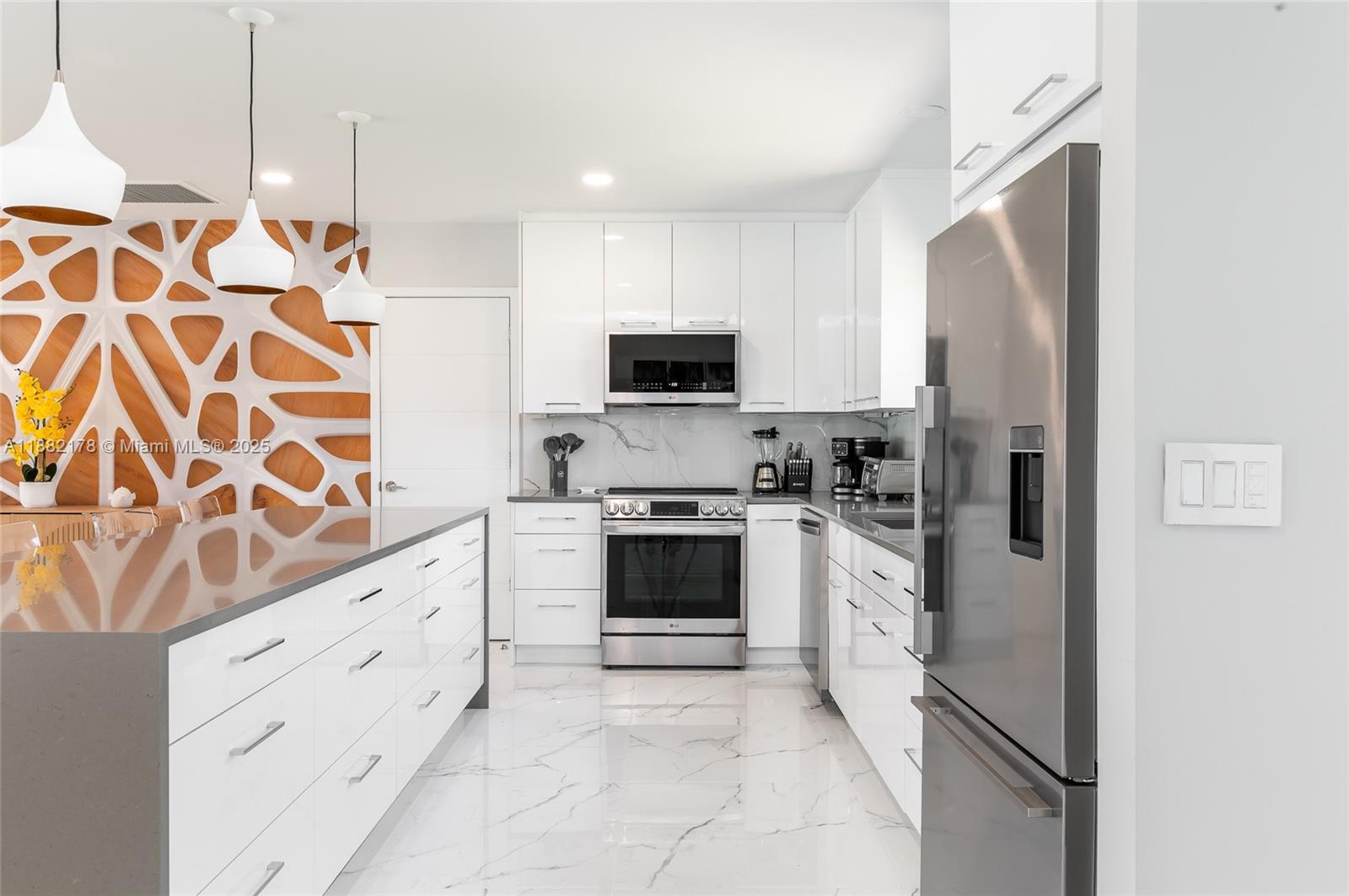 A modern kitchen features white cabinets, stainless steel appliances, and a decorative wood-patterned wall — 21230 NE 25th Ct, Miami FL 33180, MIAMI, FL