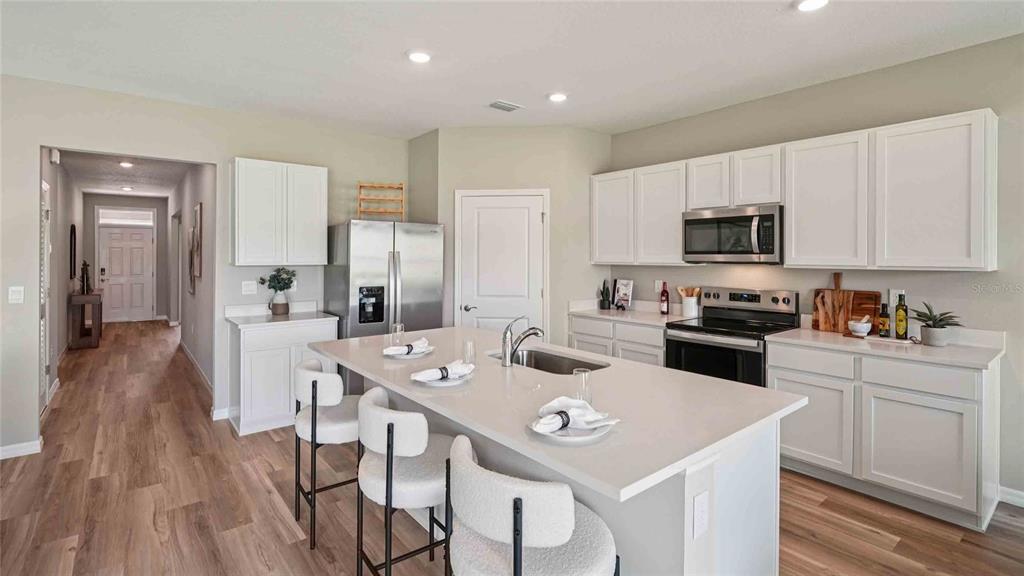 A modern kitchen features white cabinetry, stainless steel appliances, a quartz island, and wood flooring — 24274 NW 13TH BOULEVARD, NEWBERRY, FL