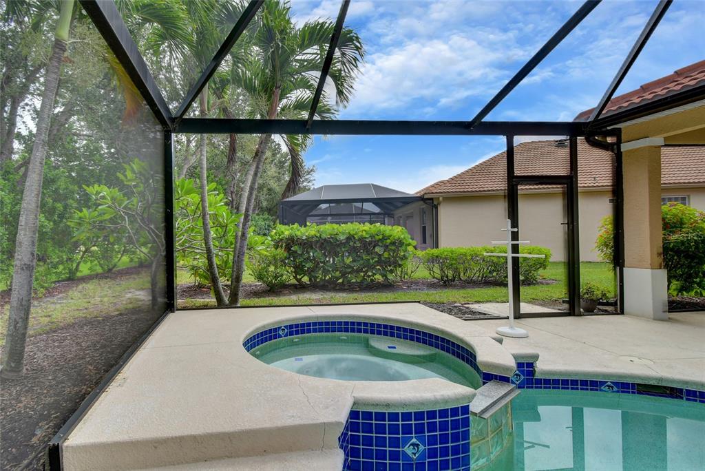A screened-in patio features a tiled hot tub and swimming pool overlooking a landscaped yard — 17899 COURTSIDE LANDINGS CIRCLE, PUNTA GORDA, FL