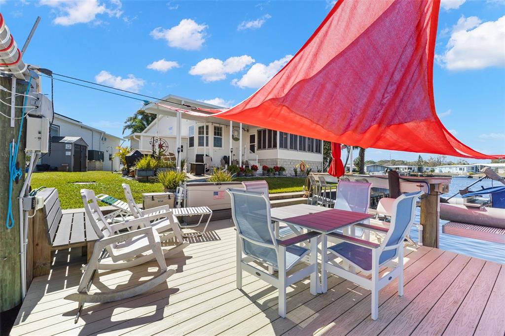 A wooden deck features outdoor dining furniture and a large red shade sail by water — 7166 MOUNT ARLINGTON DRIVE NE UNIT 418, ST PETERSBURG, FL