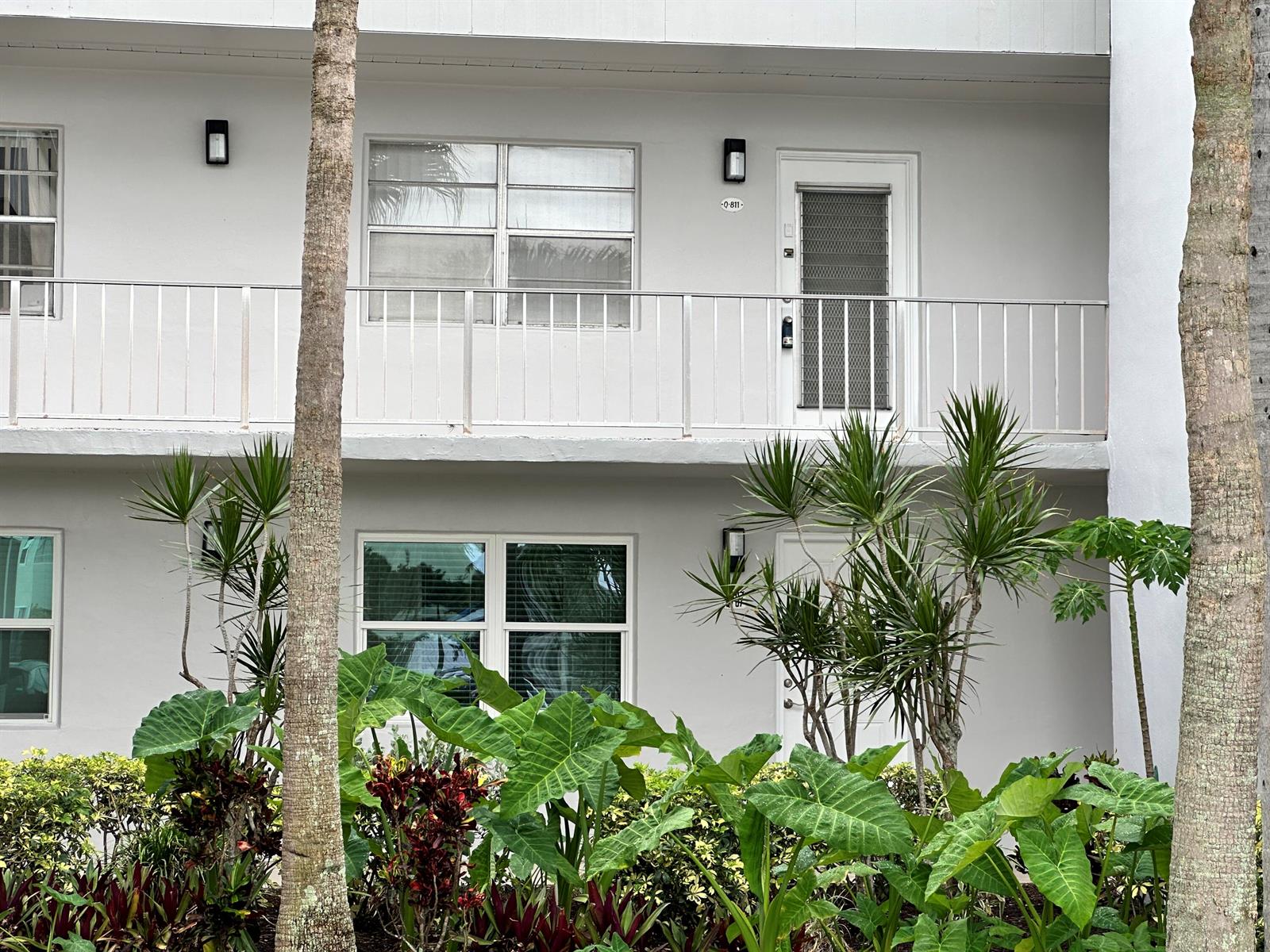 A two-story apartment building exterior features a balcony, white walls, and lush tropical landscaping — 811 Flanders Q, Delray Beach FL 33484, DELRAY BEACH, FL