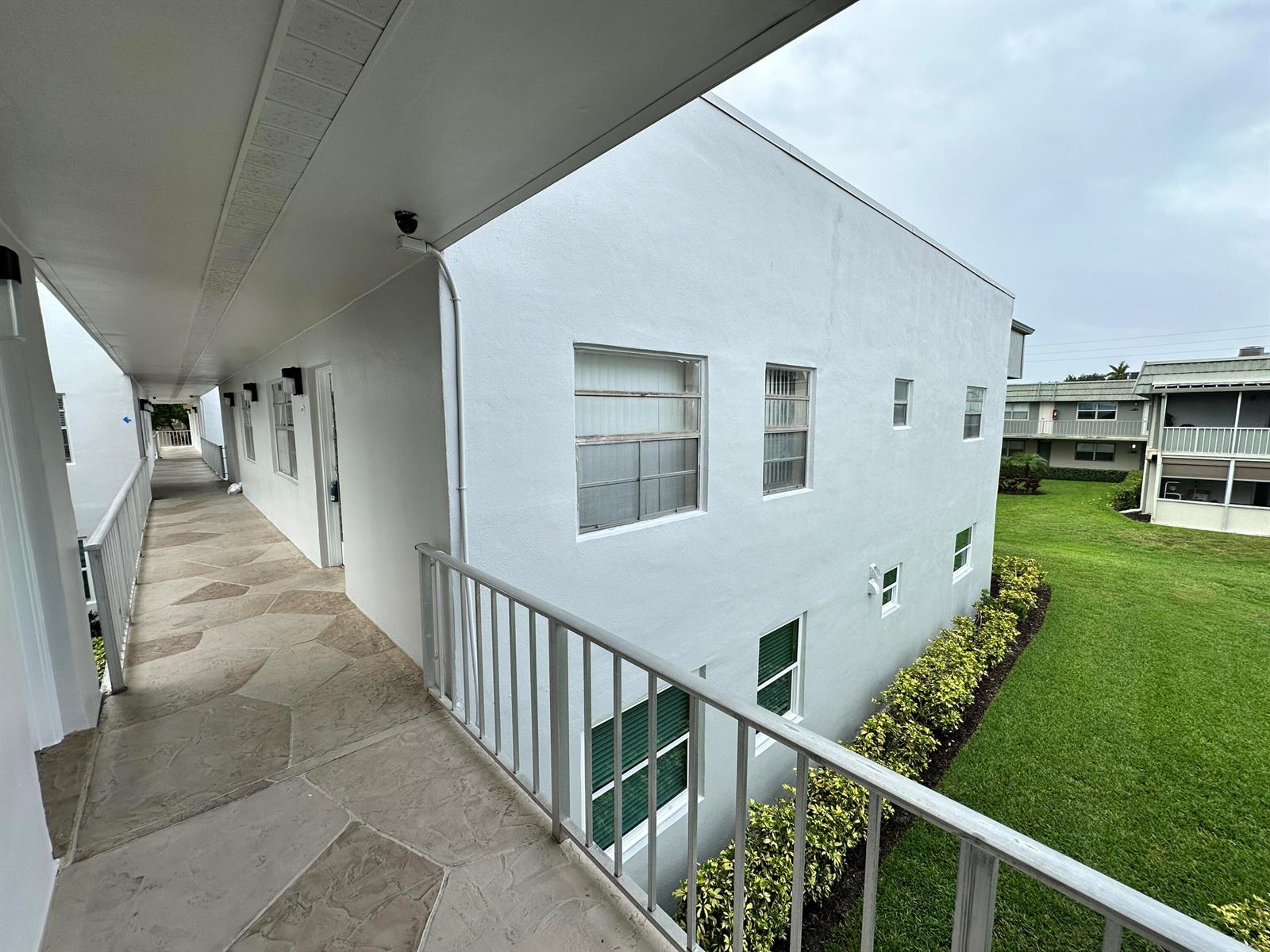 An exterior view of a multi-story apartment building with a concrete walkway and metal railing — 811 Flanders Q, Delray Beach FL 33484, DELRAY BEACH, FL