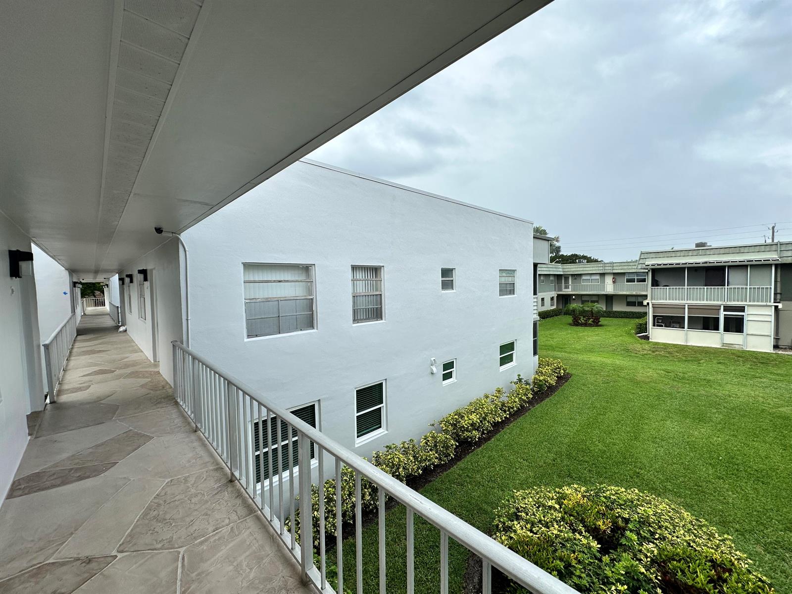 An exterior view of an apartment complex with a walkway overlooking a grassy courtyard — 811 Flanders Q, Delray Beach FL 33484, DELRAY BEACH, FL