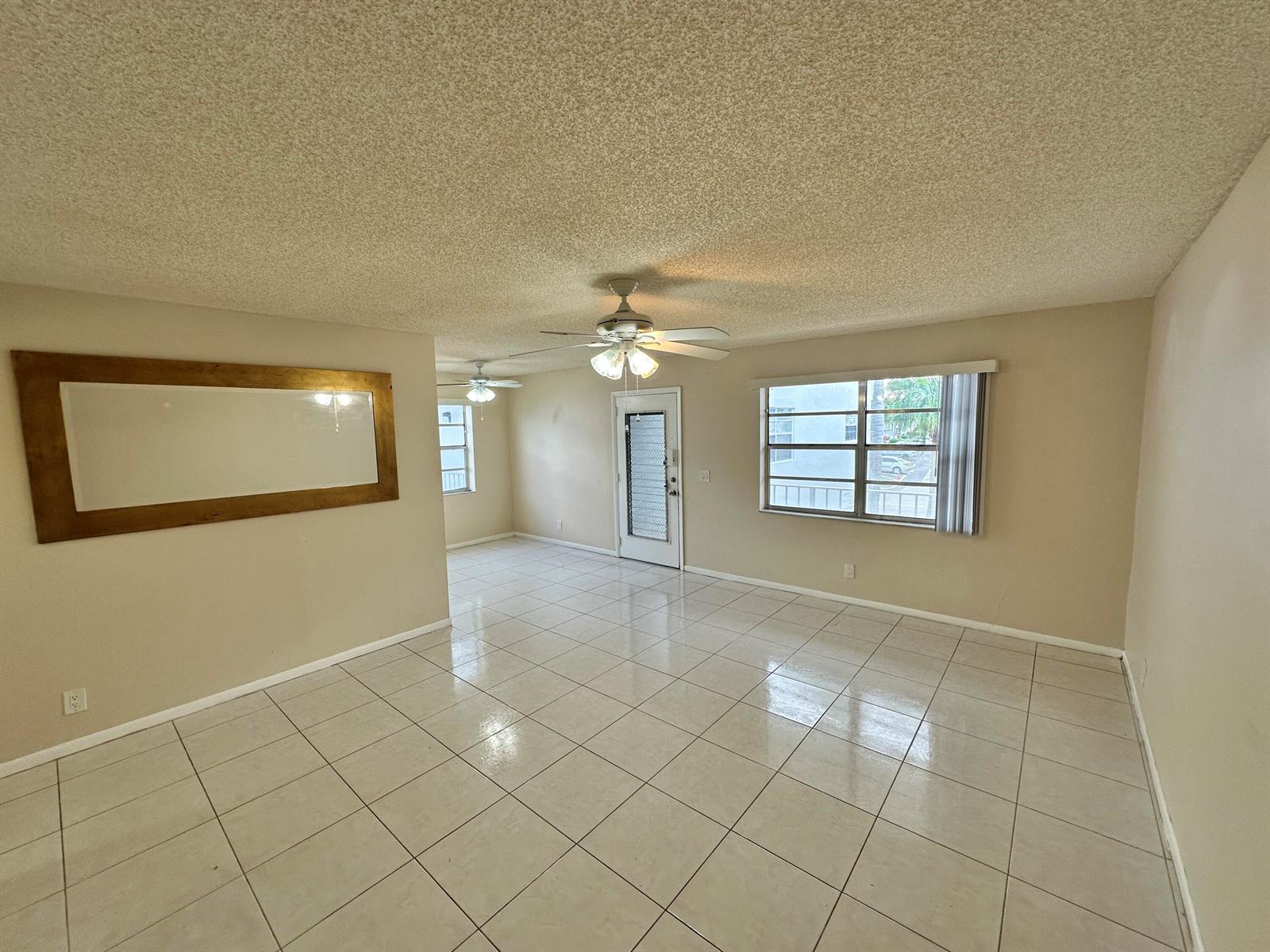 An empty living area features beige walls, a popcorn ceiling, and light-colored tile flooring — 811 Flanders Q, Delray Beach FL 33484, DELRAY BEACH, FL