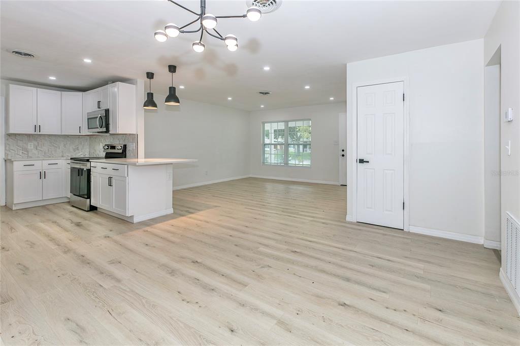 A bright, open-concept kitchen and living area featuring white cabinetry and light wood-look flooring — 1842 PURITAN AVENUE, WINTER PARK, FL