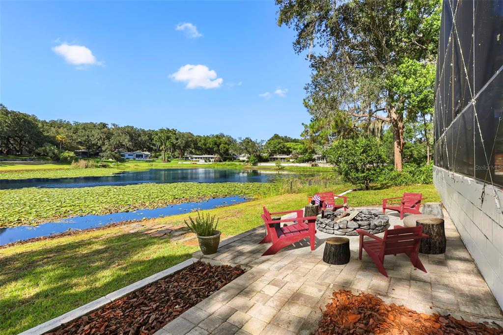 A stone patio with red chairs and a fire pit overlooks a lily-covered pond — 1301 DRUID ISLE ROAD, MAITLAND, FL