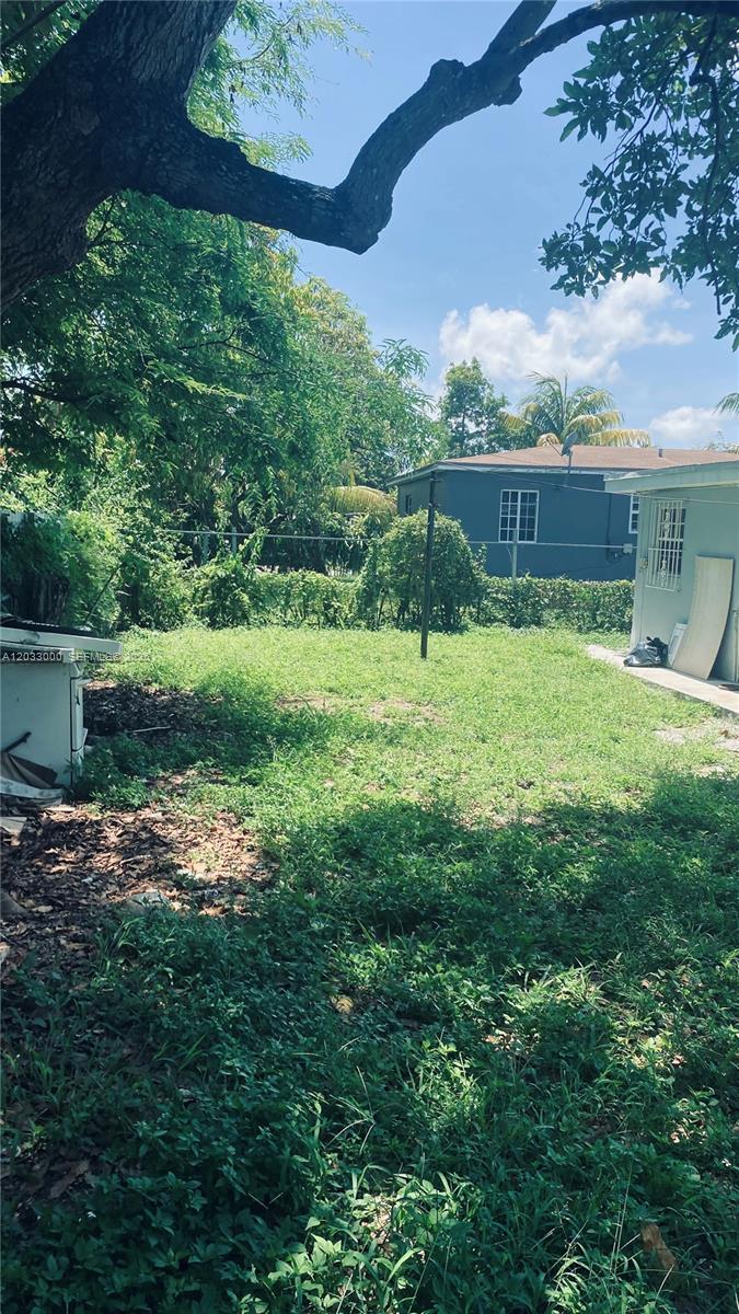 A backyard with a grassy lawn, mature trees, and a view of neighboring houses — 1120 NW 147th St # 0, Miami FL 33168, MIAMI, FL