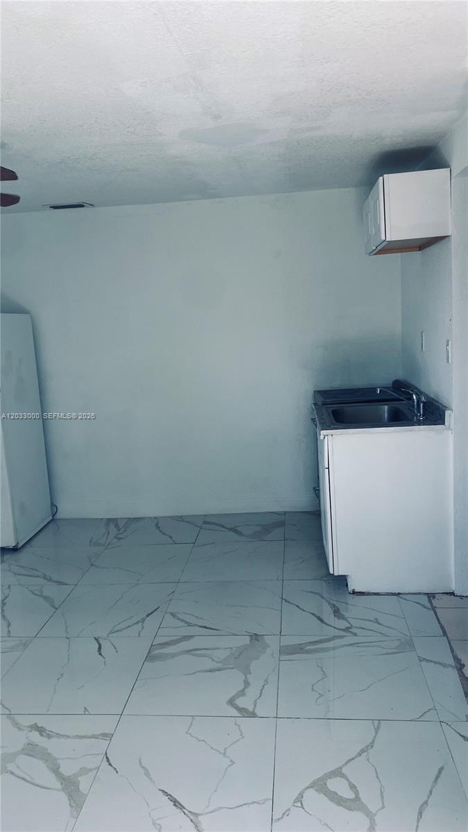 A small kitchen area features white cabinets, a sink, and light-colored marble-patterned floor tiles — 1120 NW 147th St # 0, Miami FL 33168, MIAMI, FL