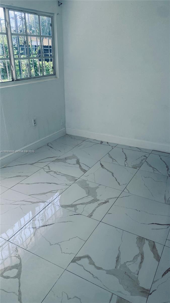 An empty room features white walls, a window with security bars, and marble-patterned tile flooring — 1120 NW 147th St # 0, Miami FL 33168, MIAMI, FL