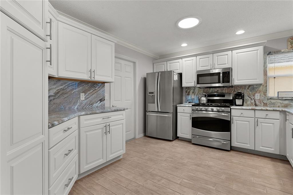 A kitchen features white cabinets, stainless steel appliances, and a patterned stone backsplash — 1536 BARNWELL PLACE, THE VILLAGES, FL