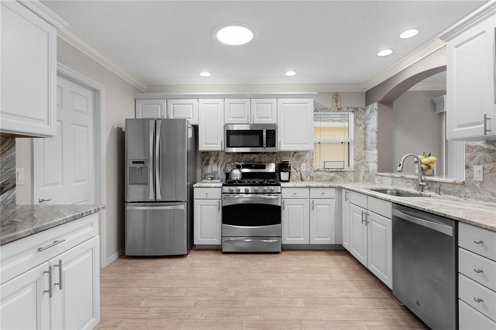 A kitchen with white cabinets, stainless steel appliances, and marble-patterned countertops and backsplash — 1536 BARNWELL PLACE, THE VILLAGES, FL