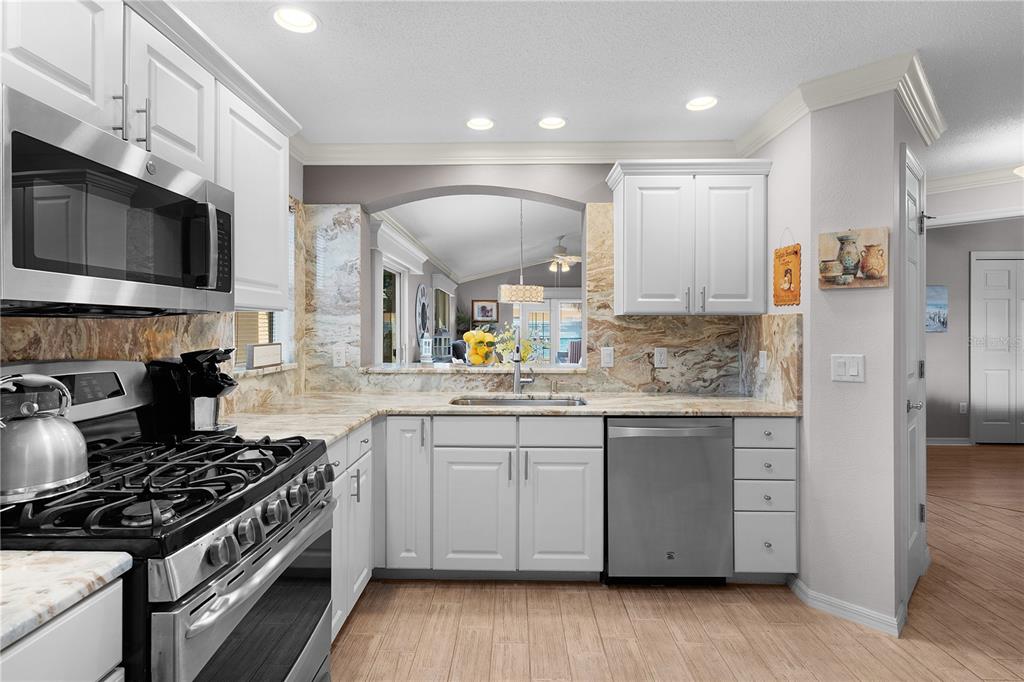 A kitchen features white cabinets, stainless steel appliances, and a marble-patterned backsplash and countertop — 1536 BARNWELL PLACE, THE VILLAGES, FL