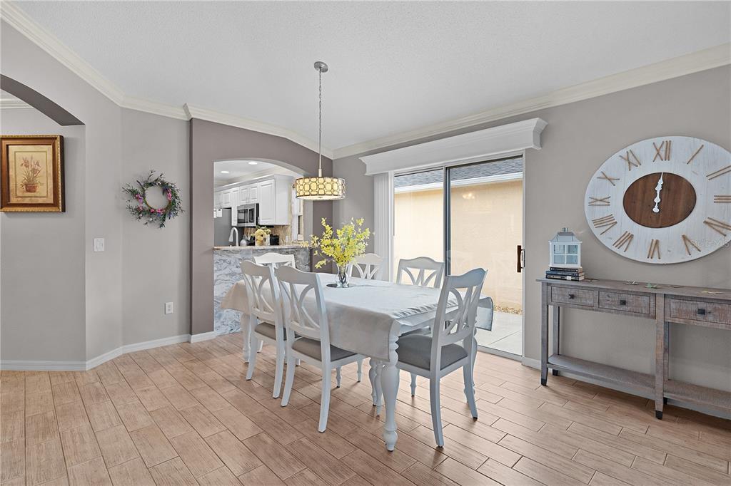 A dining room with a table, chairs, a large wall clock, and a sliding glass door — 1536 BARNWELL PLACE, THE VILLAGES, FL