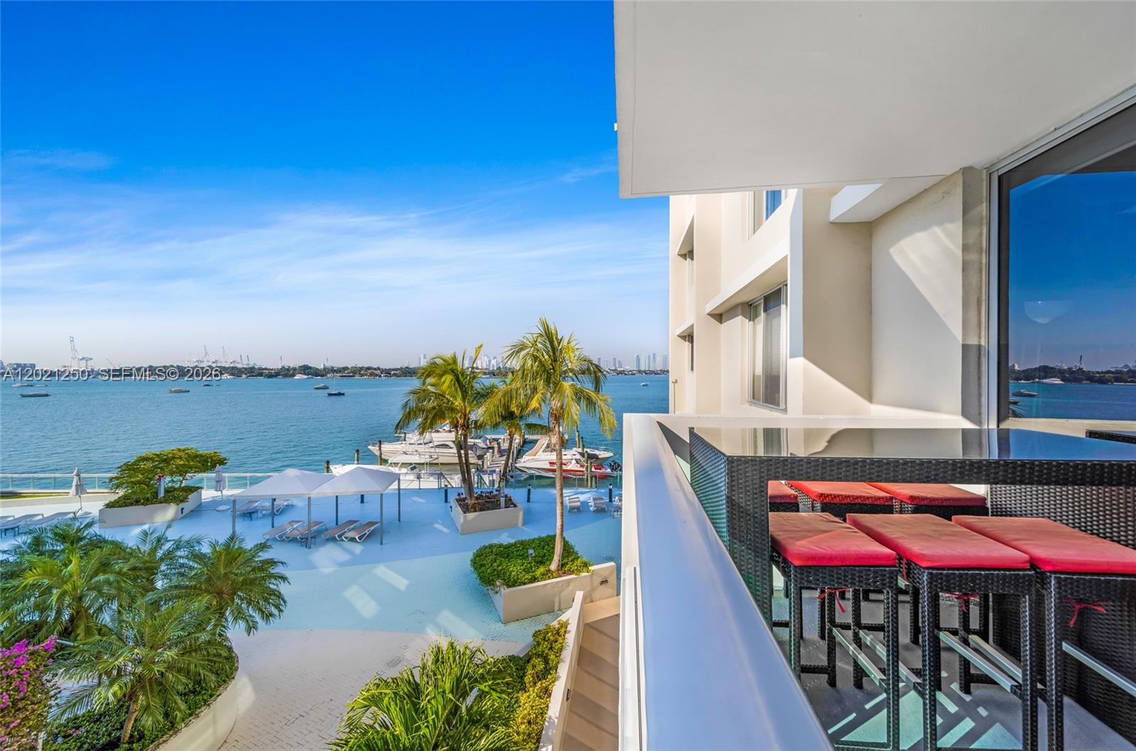 A balcony with a high-top table and red stools overlooks a pool deck and bay — 1200 West Ave # 327, Miami Beach FL 33139, MIAMI BEACH, FL