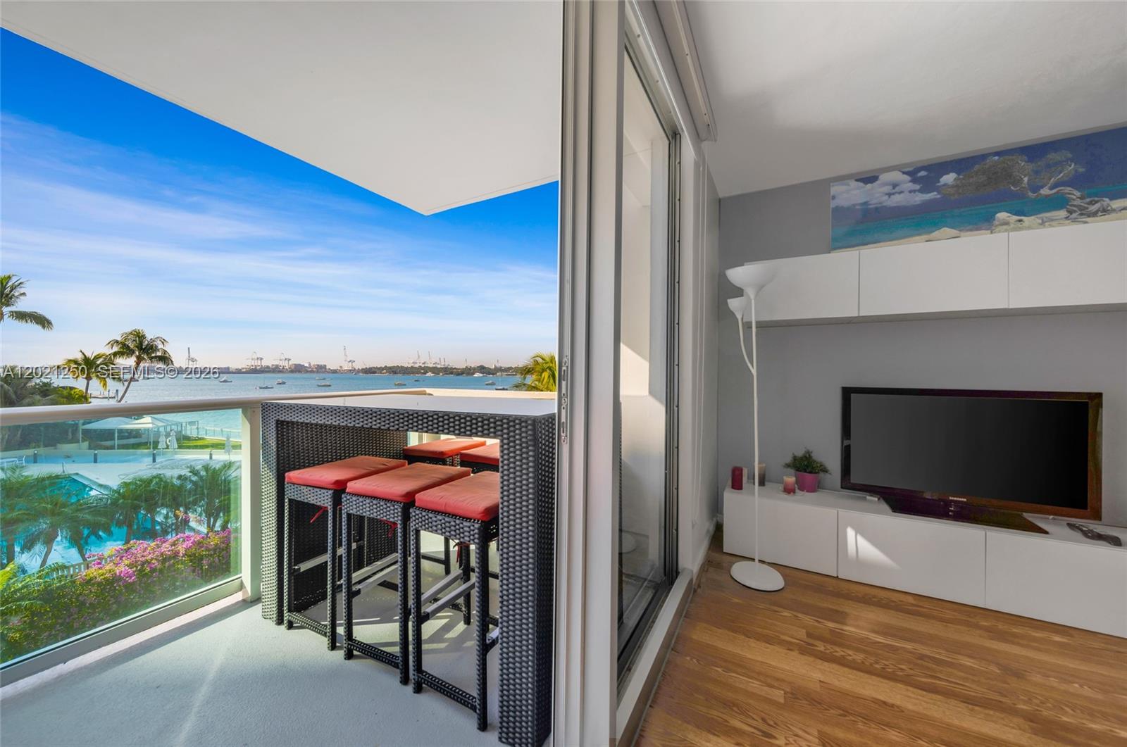 A balcony with a high-top table overlooks the water next to a living room — 1200 West Ave # 327, Miami Beach FL 33139, MIAMI BEACH, FL