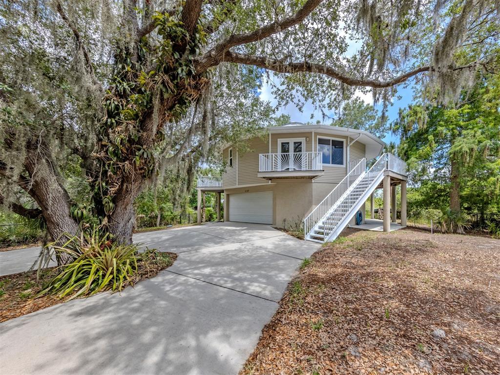 A two-story circular house with a garage, elevated deck, and exterior staircase under large trees — 11883 DE LEON DRIVE, NORTH PORT, FL
