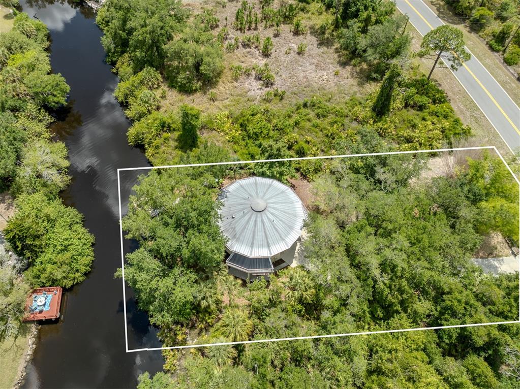 An aerial view shows a circular house with a metal roof surrounded by dense trees — 11883 DE LEON DRIVE, NORTH PORT, FL