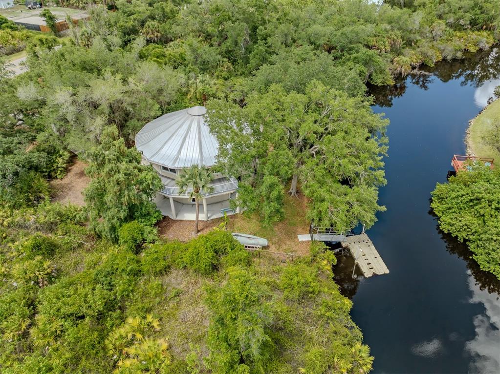 An aerial view shows a round house with a metal roof nestled among trees by water — 11883 DE LEON DRIVE, NORTH PORT, FL