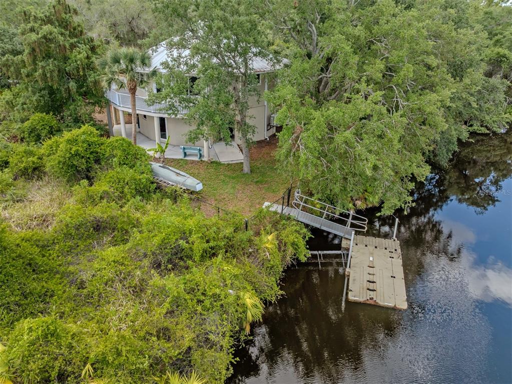 An aerial view shows a two-story house with a balcony, dock, and kayak by water — 11883 DE LEON DRIVE, NORTH PORT, FL