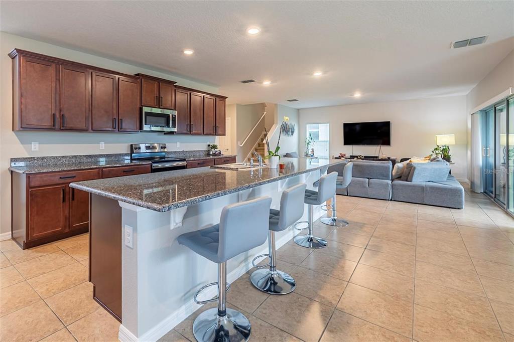 A kitchen with dark wood cabinets and granite countertops features a breakfast bar with stools — 565 OGELTHORPE DRIVE, DAVENPORT, FL