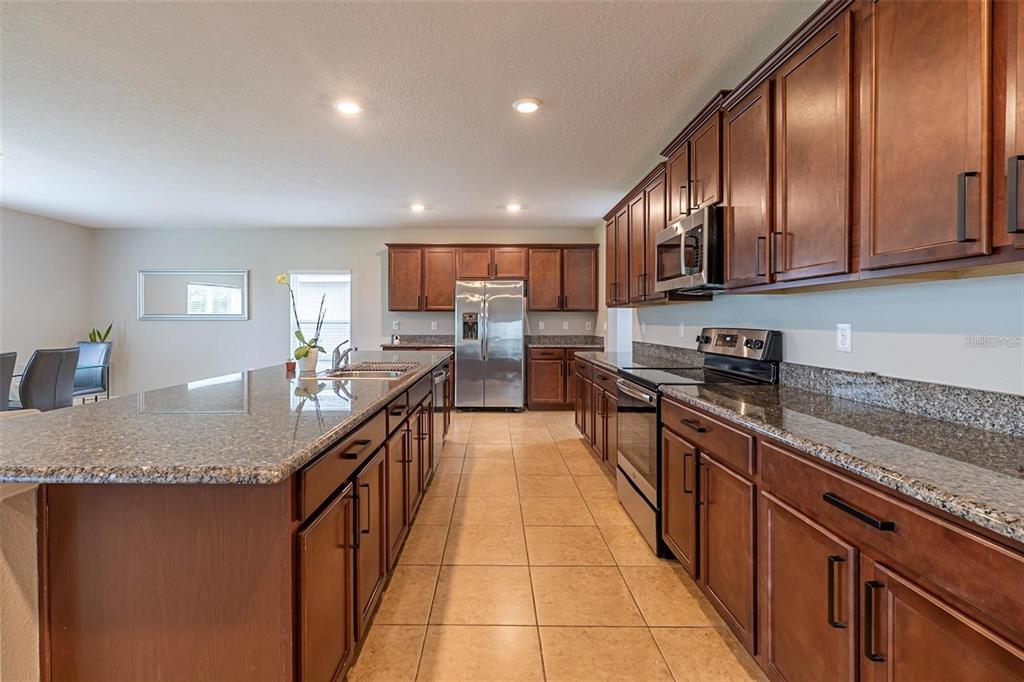 A kitchen with dark wood cabinets, granite countertops, stainless steel appliances, and tile flooring — 565 OGELTHORPE DRIVE, DAVENPORT, FL