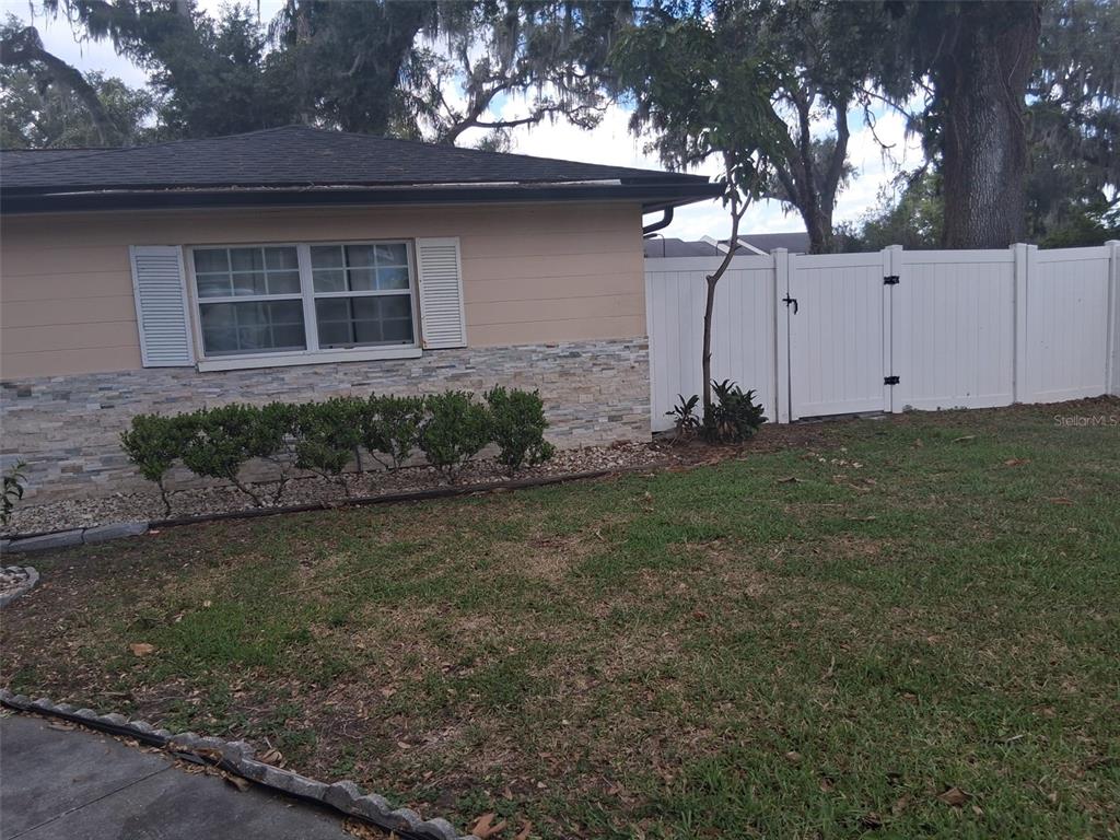 A tan house with stone siding and white shutters sits next to a white fence — 702 COULTER PLACE, BRANDON, FL