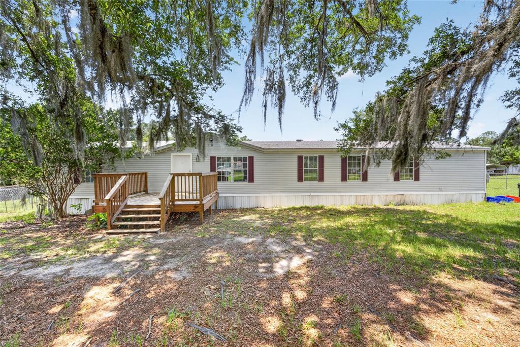 A single-story manufactured home with light gray siding and a wooden deck entrance — 13530 SW 87TH STREET, ARCHER, FL