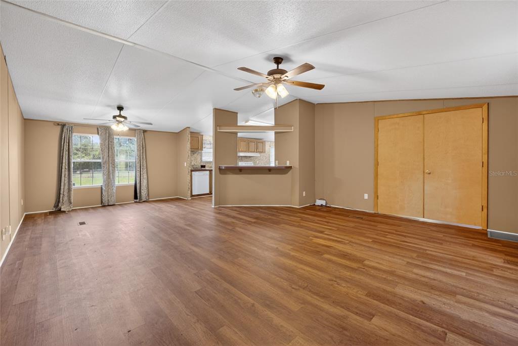 A spacious living room features wood-look flooring, tan walls, a ceiling fan, and a breakfast bar — 13530 SW 87TH STREET, ARCHER, FL