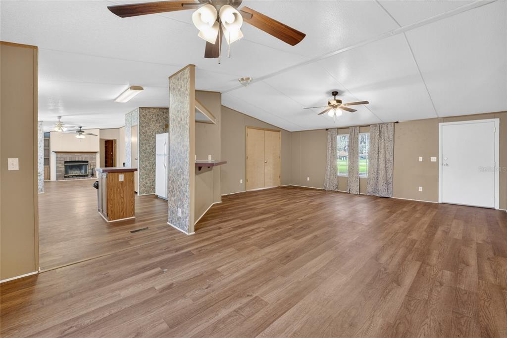 A spacious living area with wood-look flooring, a ceiling fan, and an adjacent kitchen space — 13530 SW 87TH STREET, ARCHER, FL