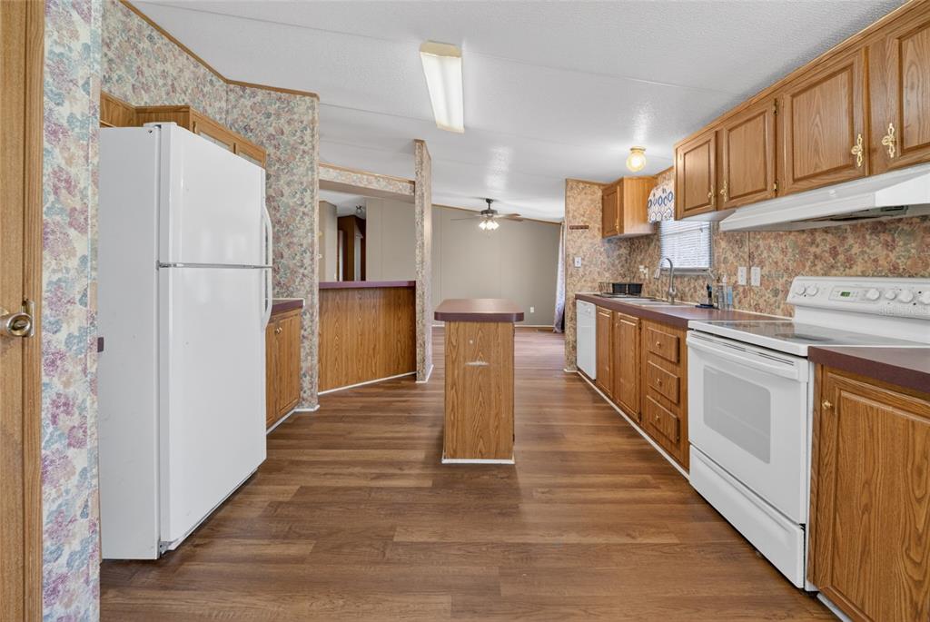 A kitchen with wood cabinets, white appliances, floral wallpaper, and a small central island — 13530 SW 87TH STREET, ARCHER, FL