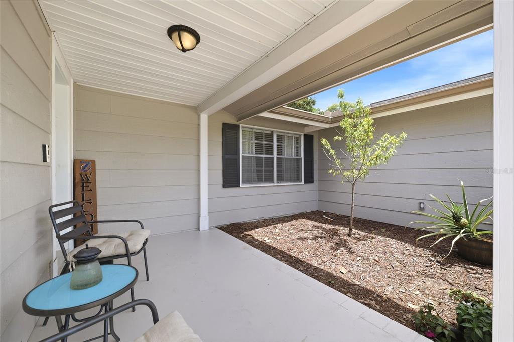 A covered patio features a small garden bed, a bistro set, and a welcome sign — 12408 STAGECOACH LANE, HUDSON, FL