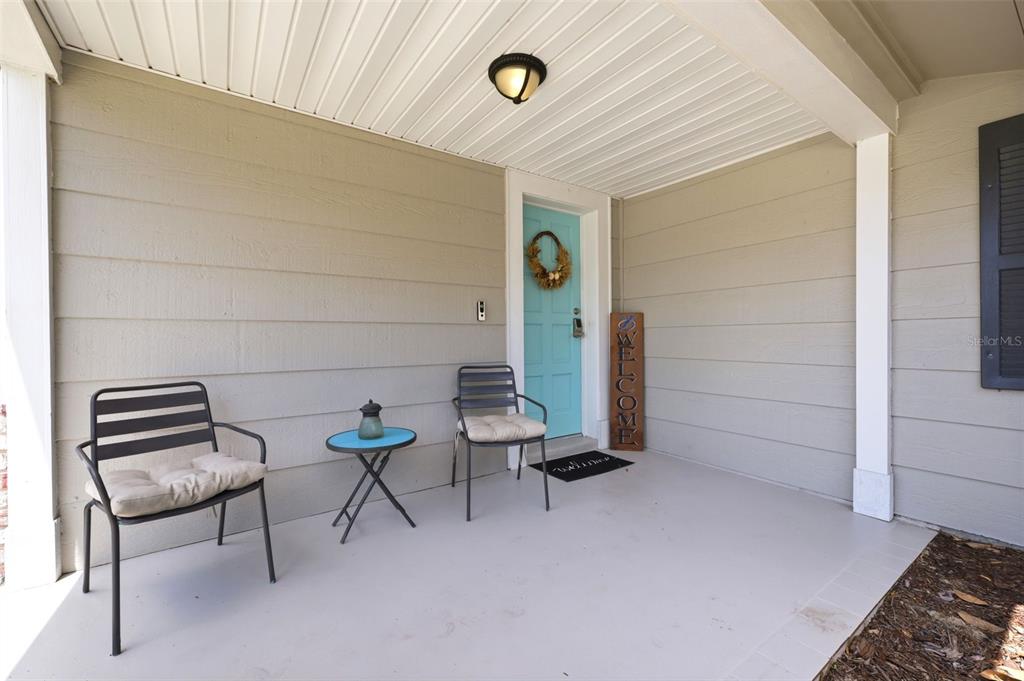 A covered front porch features a light blue door, two metal chairs, and a table — 12408 STAGECOACH LANE, HUDSON, FL