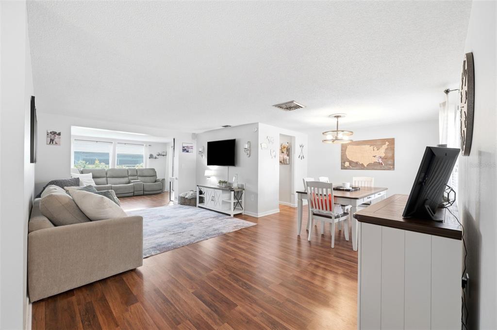 An open-concept living and dining area features wood-look flooring, white walls, and a ceiling fan — 12408 STAGECOACH LANE, HUDSON, FL
