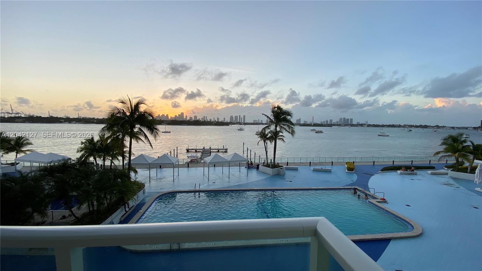 A balcony view overlooks a swimming pool, palm trees, and a bay with a city skyline — 1000 WEST AVE # 318, Miami Beach FL 33139, MIAMI BEACH, FL