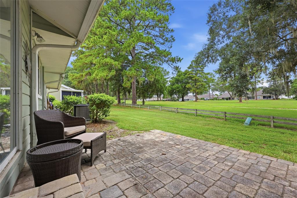 A paved patio with outdoor furniture overlooks a grassy backyard and a wooden fence — 1022 NW 125TH DRIVE, NEWBERRY, FL