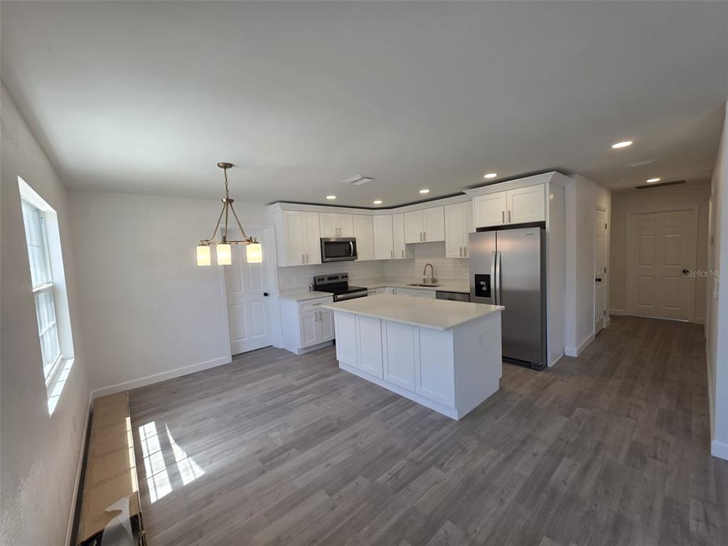 A modern kitchen features white cabinetry, stainless steel appliances, a central island, and wood-look flooring — 1401 PENNSYLVANIA AVENUE, CLEARWATER, FL