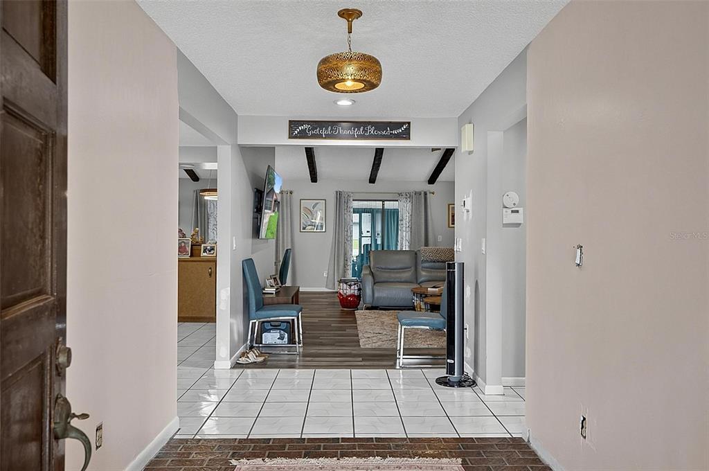 A tiled entryway leads into a living room with wood-look flooring and exposed ceiling beams — 3 BLAKE COURT, PALM COAST, FL