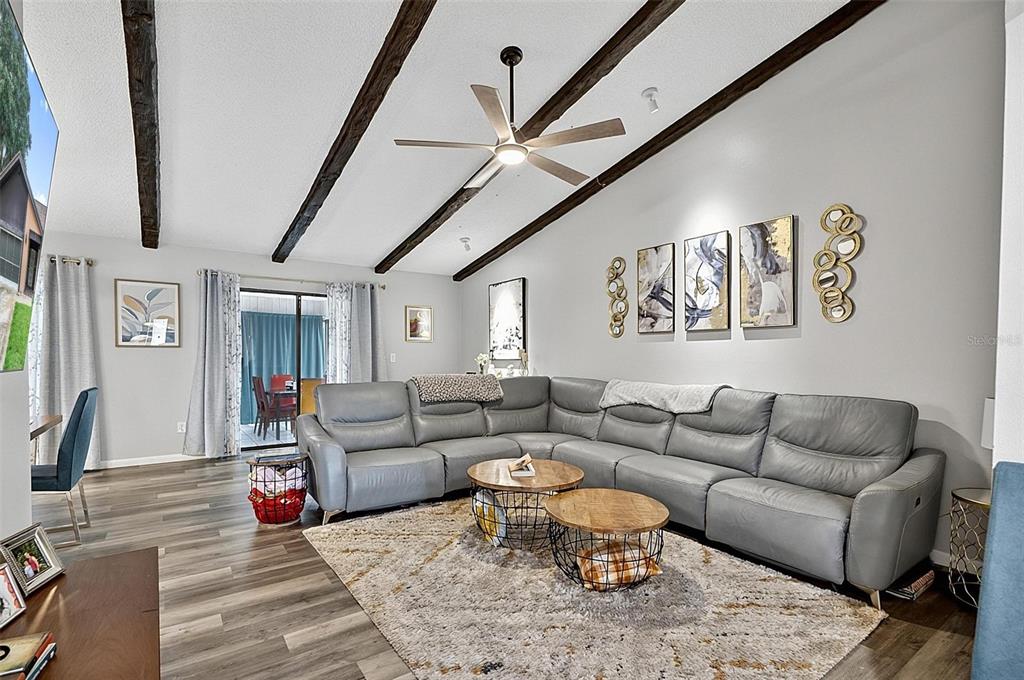 A living room features a gray sectional sofa, wood-look flooring, and exposed ceiling beams — 3 BLAKE COURT, PALM COAST, FL